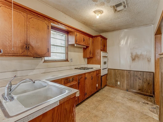 kitchen featuring sink, white appliances, a textured ceiling, and wooden walls