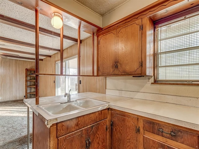 kitchen with sink, kitchen peninsula, a textured ceiling, wooden walls, and carpet