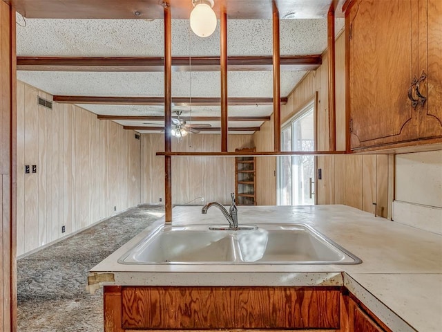 kitchen featuring beamed ceiling, ceiling fan, wood walls, and sink