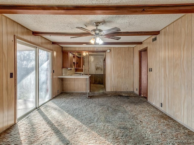 unfurnished living room with beam ceiling, a textured ceiling, ceiling fan, and wood walls