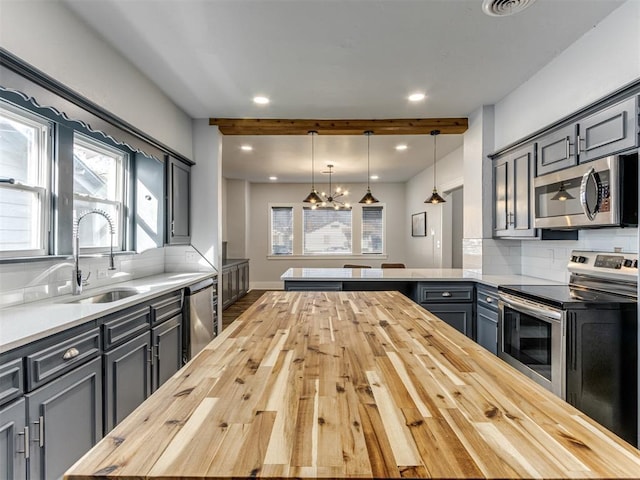 kitchen featuring decorative backsplash, appliances with stainless steel finishes, wood counters, sink, and hanging light fixtures