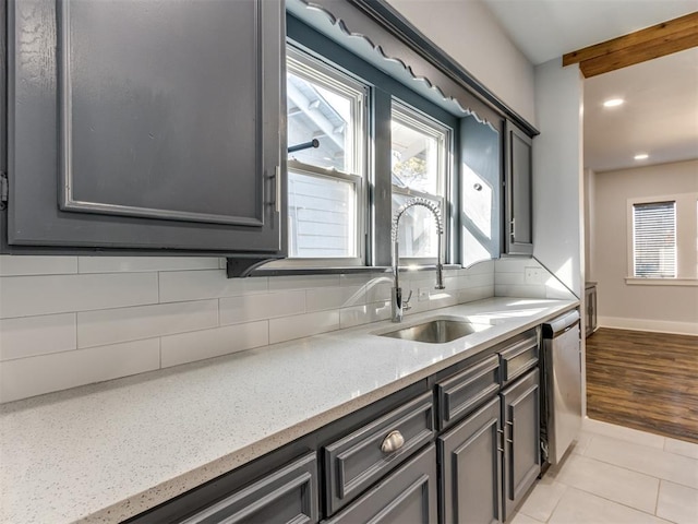 kitchen featuring backsplash, sink, stainless steel dishwasher, light stone countertops, and light tile patterned flooring