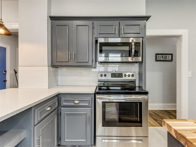 kitchen with decorative backsplash, appliances with stainless steel finishes, gray cabinets, and light hardwood / wood-style flooring