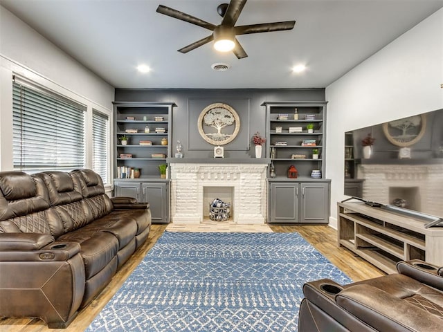 living room featuring built in shelves, ceiling fan, light wood-type flooring, and a fireplace