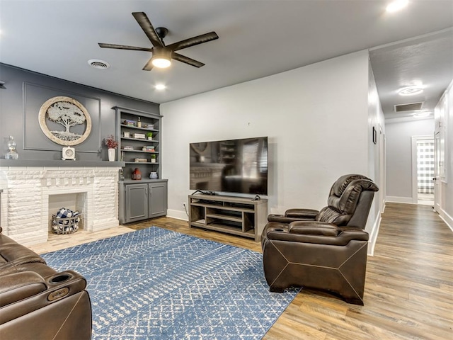 living room featuring hardwood / wood-style floors, built in shelves, ceiling fan, and a fireplace