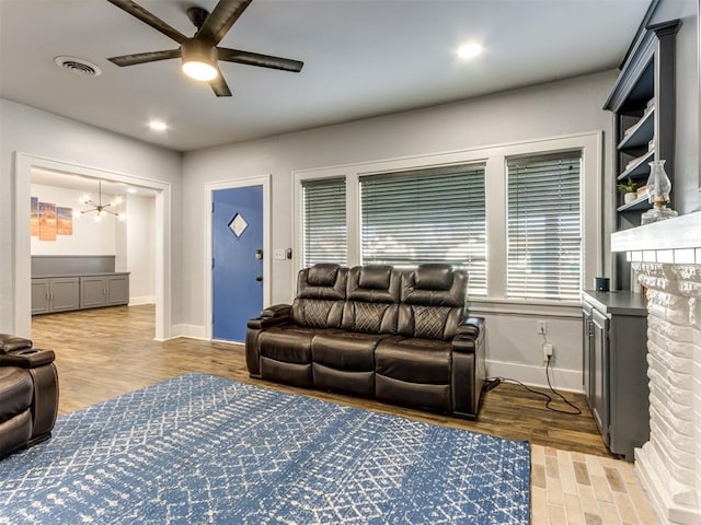 living room featuring a fireplace, ceiling fan with notable chandelier, and light wood-type flooring