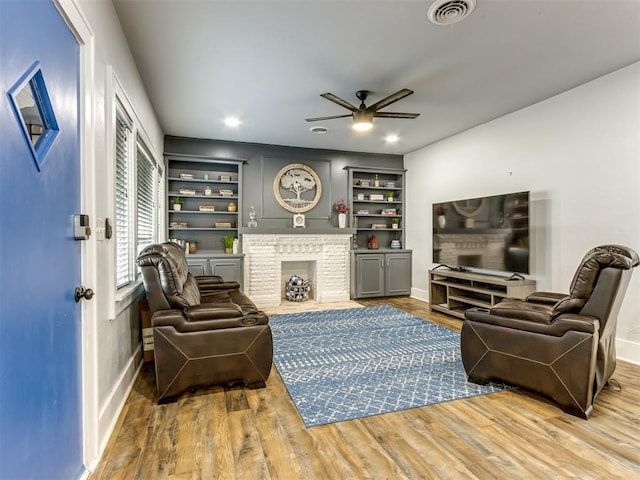 living room with built in features, hardwood / wood-style floors, and a brick fireplace