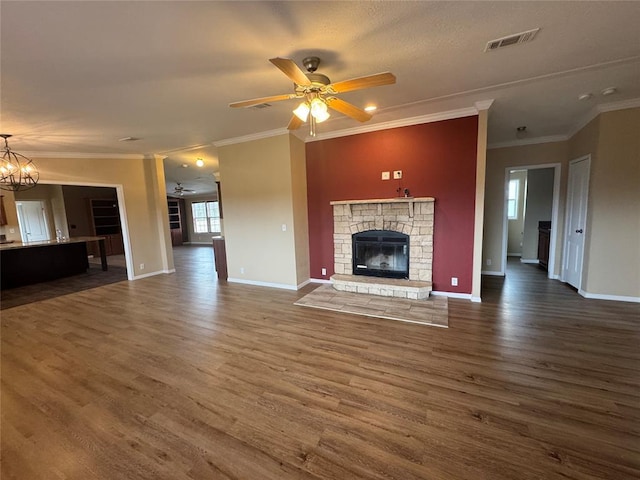 unfurnished living room featuring ceiling fan with notable chandelier, dark hardwood / wood-style floors, a stone fireplace, and crown molding