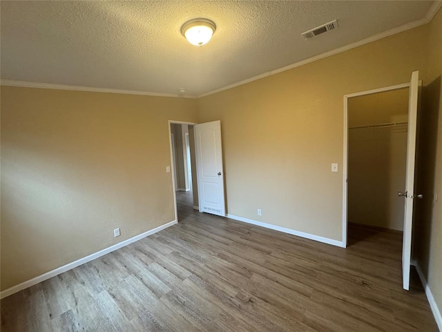 unfurnished bedroom with a spacious closet, hardwood / wood-style floors, a textured ceiling, a closet, and ornamental molding