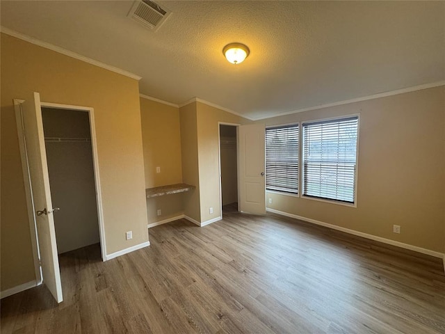 unfurnished bedroom featuring crown molding, built in desk, a textured ceiling, and light wood-type flooring