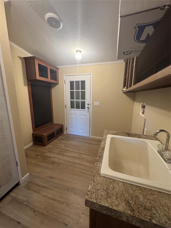 kitchen with a textured ceiling, ornamental molding, sink, and hardwood / wood-style flooring