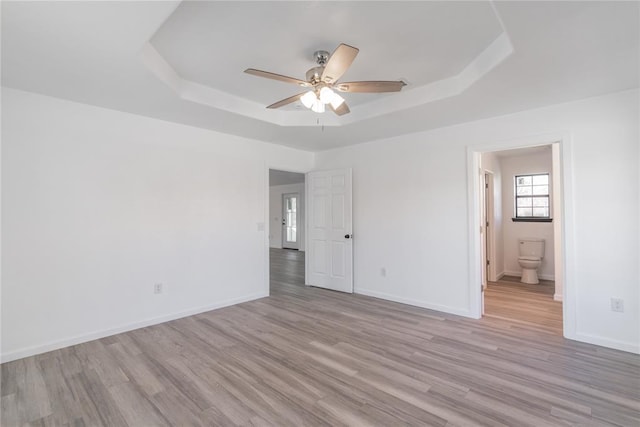 empty room featuring ceiling fan, light wood-type flooring, and a tray ceiling