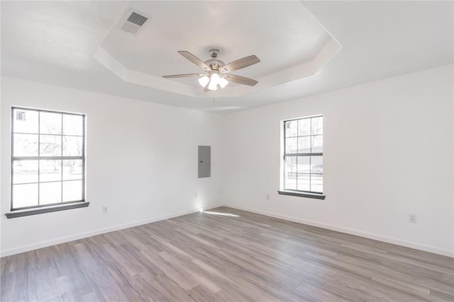 spare room featuring light hardwood / wood-style floors, electric panel, and a tray ceiling