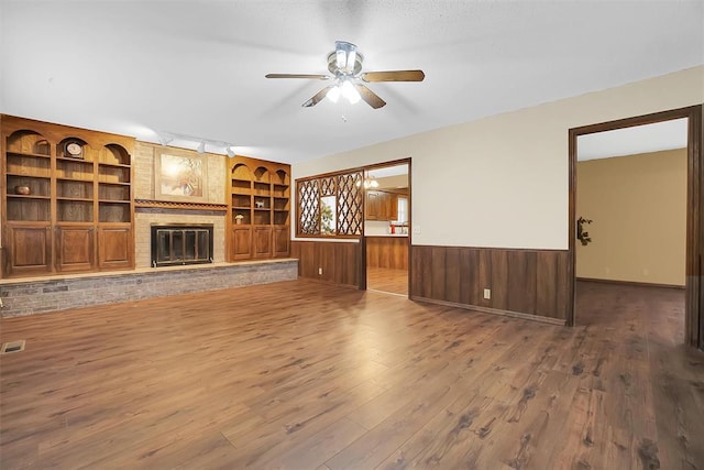 unfurnished living room with built in features, hardwood / wood-style flooring, a brick fireplace, and ceiling fan