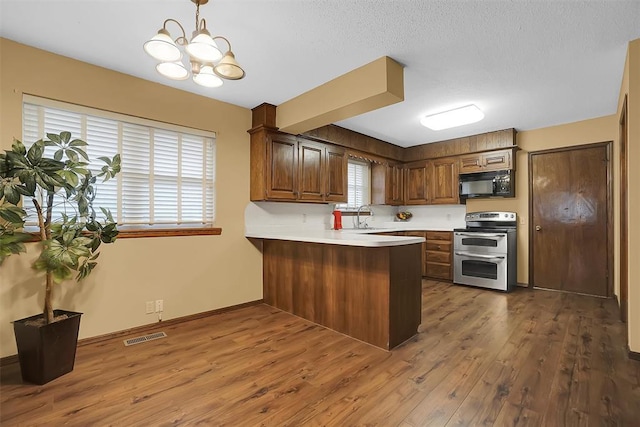 kitchen featuring sink, kitchen peninsula, pendant lighting, double oven range, and dark hardwood / wood-style floors