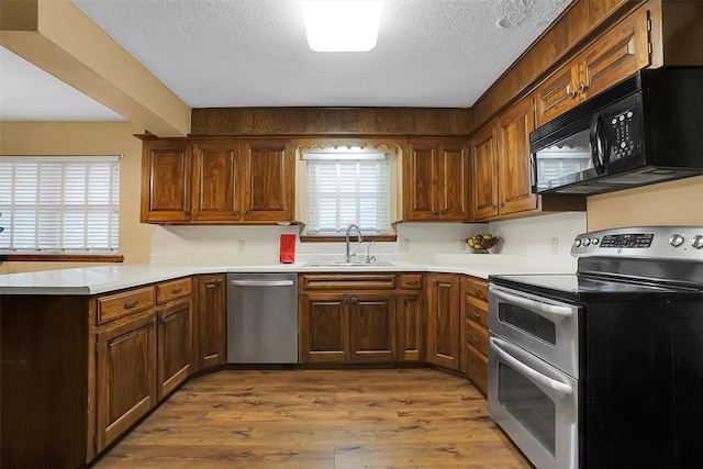 kitchen featuring sink, light wood-type flooring, a textured ceiling, and appliances with stainless steel finishes