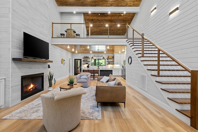 living room featuring beam ceiling, a tiled fireplace, light hardwood / wood-style flooring, and a towering ceiling