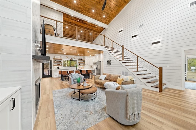 living area featuring stairway, wooden walls, light wood-type flooring, a premium fireplace, and high vaulted ceiling
