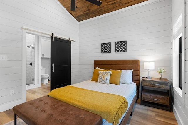 bedroom with wooden walls, a barn door, lofted ceiling, and light wood-type flooring