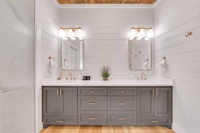 full bath with wooden walls, double vanity, a sink, and wood finished floors