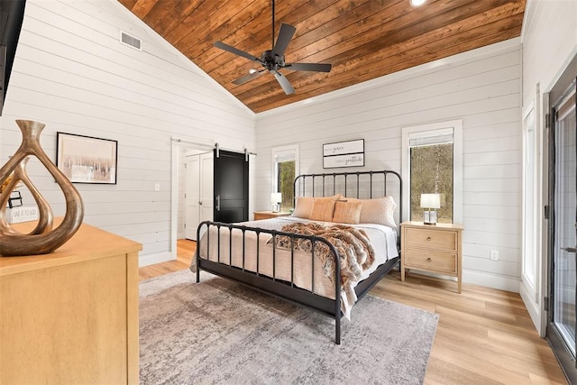 bedroom with wooden ceiling, a barn door, wooden walls, visible vents, and light wood-style flooring