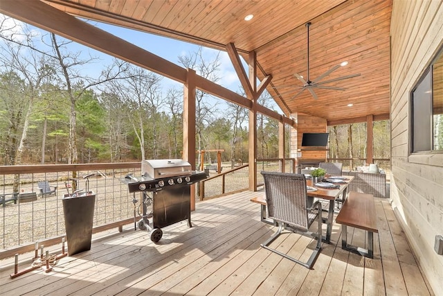 wooden terrace with outdoor dining space, ceiling fan, a grill, and a fireplace