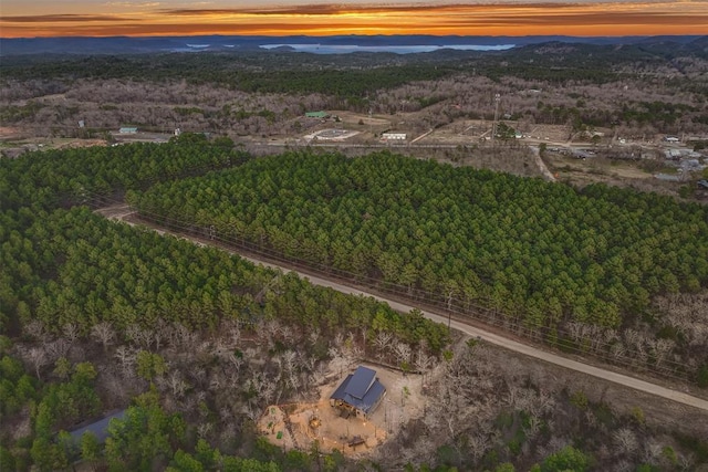 aerial view at dusk featuring a wooded view and a mountain view