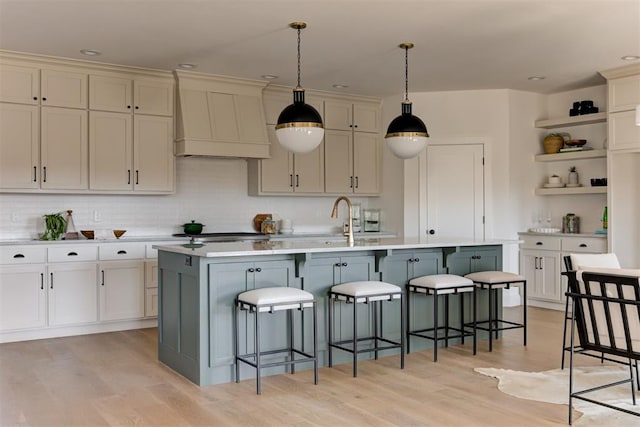 kitchen featuring light hardwood / wood-style flooring, a kitchen breakfast bar, an island with sink, custom range hood, and pendant lighting