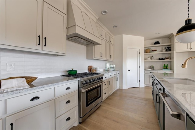 kitchen featuring premium range hood, sink, light stone counters, hanging light fixtures, and stainless steel appliances