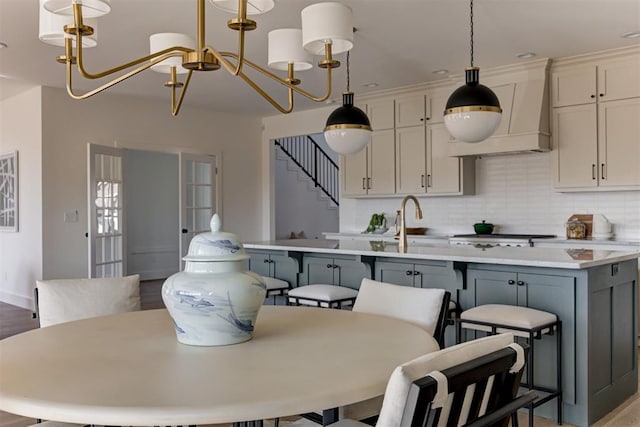 kitchen featuring gray cabinets, decorative light fixtures, a kitchen breakfast bar, custom exhaust hood, and an inviting chandelier