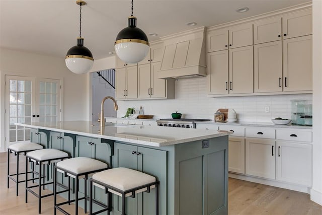 kitchen with hanging light fixtures, light stone countertops, an island with sink, custom exhaust hood, and light wood-type flooring