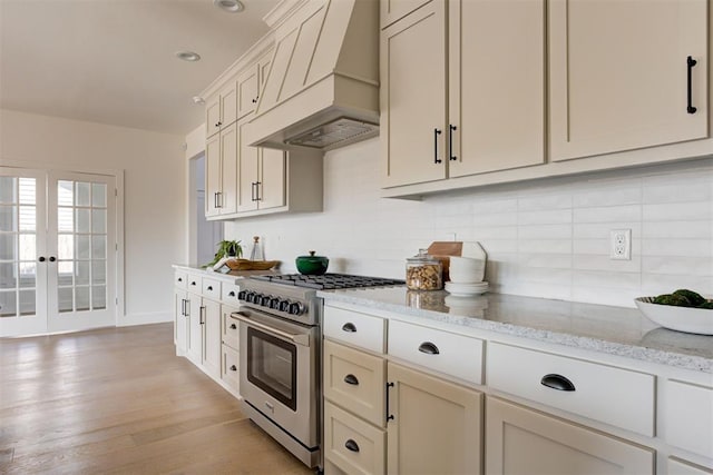 kitchen featuring light stone counters, light wood-type flooring, stainless steel stove, custom range hood, and cream cabinets