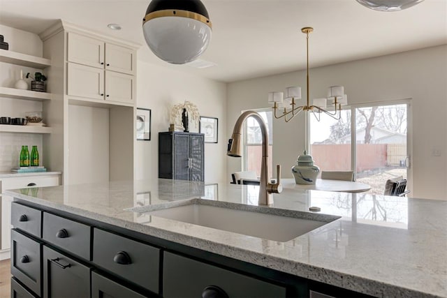 kitchen featuring decorative light fixtures, white cabinetry, sink, light stone countertops, and an inviting chandelier