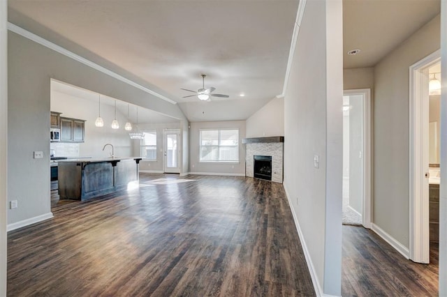 unfurnished living room featuring dark hardwood / wood-style flooring, vaulted ceiling, ceiling fan, sink, and a fireplace