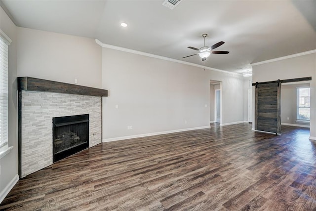 unfurnished living room with crown molding, dark hardwood / wood-style floors, a barn door, ceiling fan, and a fireplace