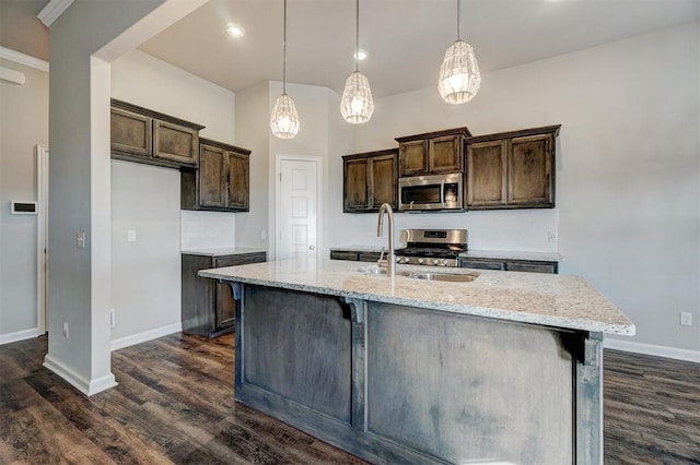 kitchen with light stone countertops, appliances with stainless steel finishes, pendant lighting, and an island with sink