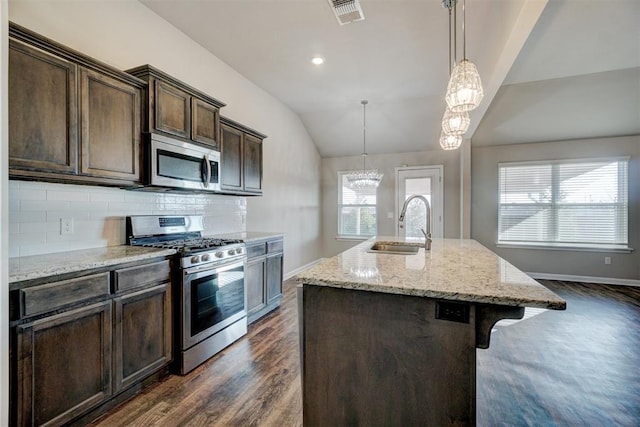 kitchen with hanging light fixtures, stainless steel appliances, tasteful backsplash, a breakfast bar area, and a center island with sink