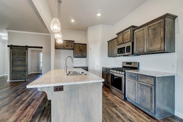 kitchen featuring sink, a barn door, an island with sink, light stone counters, and stainless steel appliances