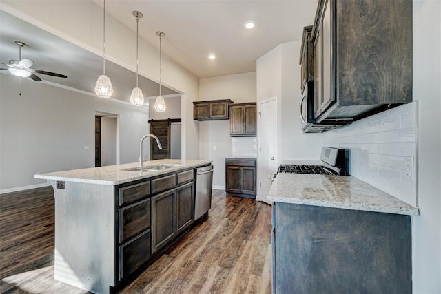 kitchen featuring decorative backsplash, appliances with stainless steel finishes, light stone countertops, sink, and a center island with sink