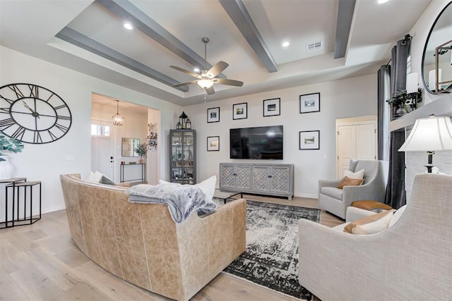 living room featuring ceiling fan with notable chandelier, light hardwood / wood-style floors, beam ceiling, and a tray ceiling