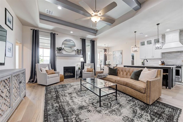 living room with a tray ceiling, ceiling fan, sink, light hardwood / wood-style flooring, and a fireplace