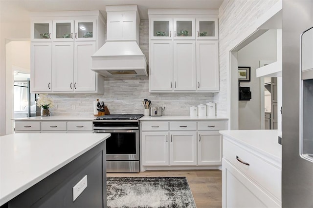 kitchen featuring tasteful backsplash, stainless steel range with electric stovetop, custom exhaust hood, light hardwood / wood-style flooring, and white cabinetry