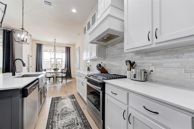 kitchen with decorative light fixtures, white cabinetry, premium range hood, and stainless steel appliances