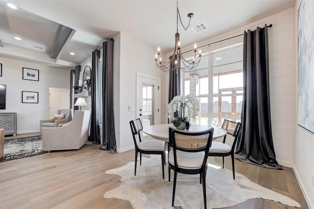 dining space featuring beamed ceiling, light hardwood / wood-style floors, and an inviting chandelier