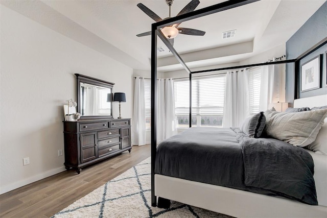 bedroom featuring a raised ceiling, ceiling fan, and light wood-type flooring