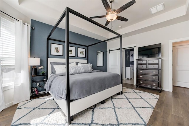 bedroom with a raised ceiling, multiple windows, ceiling fan, and wood-type flooring