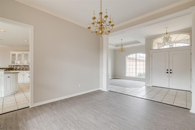 foyer with crown molding, a notable chandelier, a tray ceiling, and light wood-type flooring