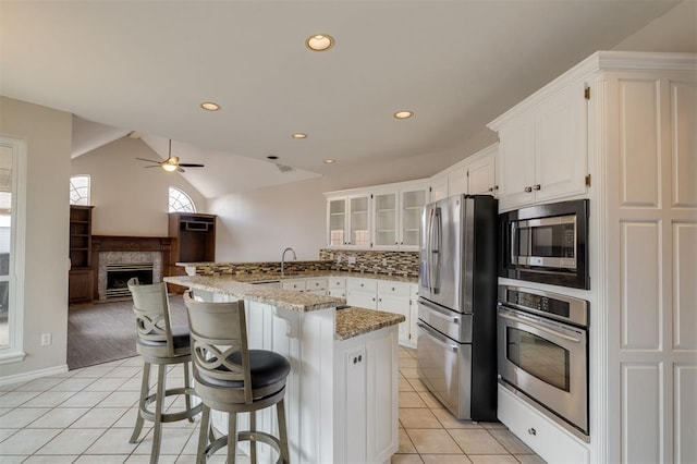 kitchen with white cabinetry, a breakfast bar area, light tile patterned floors, stainless steel appliances, and light stone countertops