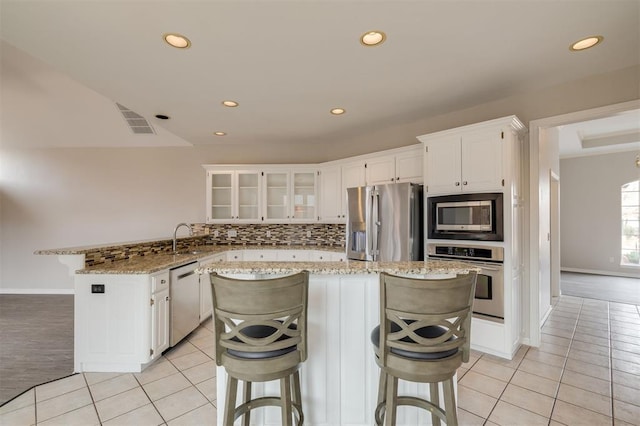 kitchen with a breakfast bar area, stainless steel appliances, a center island, light stone countertops, and white cabinets