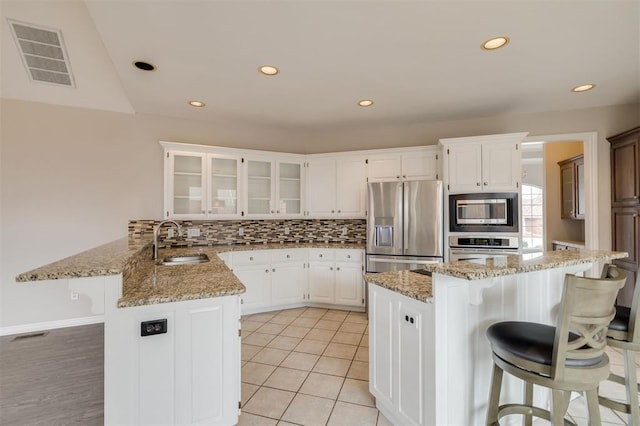 kitchen with sink, white cabinets, a kitchen breakfast bar, stainless steel appliances, and light stone countertops